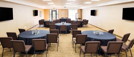 Une salle de conférence avec des tables et des chaises rondes, un sol recouvert de moquette et un grand écran mural.