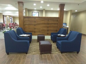 A lobby with blue armchairs, a brown ottoman, and a wooden partition wall. - Comfort Suites Piedmont - Greenville South (Piedmont)