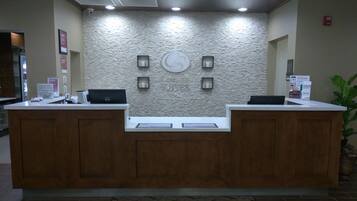 A reception desk with a stone wall backdrop, two computer monitors, and a digital screen.