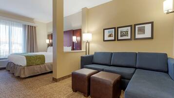 A hotel room with a bed, a sofa, two ottomans, a lamp, and three framed pictures on the wall.