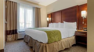 Una habitación de hotel con una cama grande, una mesita de noche con lámpara, una ventana con cortinas y un equipo de aire acondicionado.