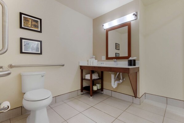 Un baño con inodoro, lavamanos, espejo y cuadros en la pared.