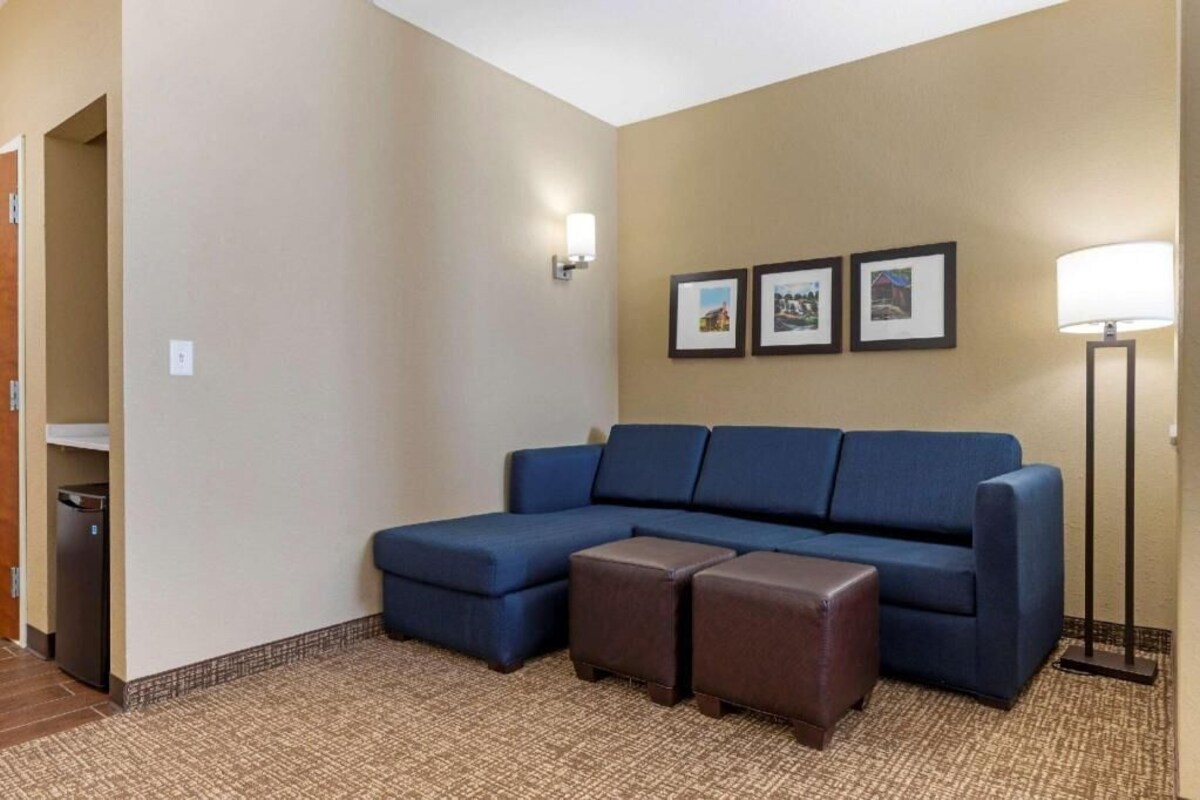 A room with a blue sectional sofa, two brown ottomans, a floor lamp, and three framed pictures on the wall.