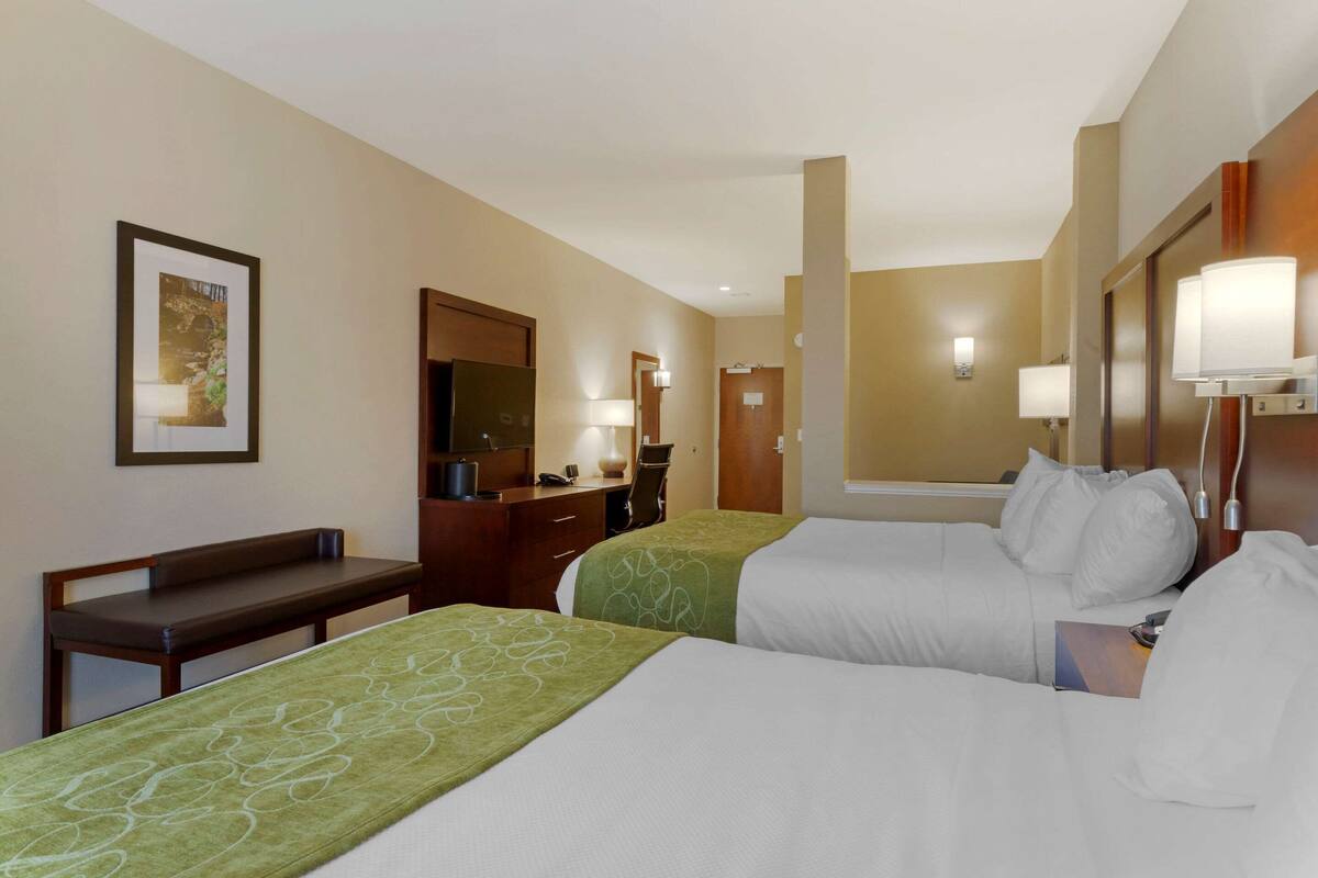 A hotel room with two beds, a desk, a chair, a mirror, and a framed picture on the wall.