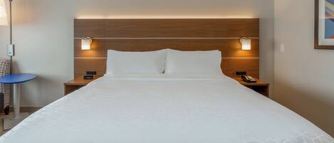 A hotel room with a large bed, two bedside tables with lamps, a small blue table, and a wall-mounted phone.
