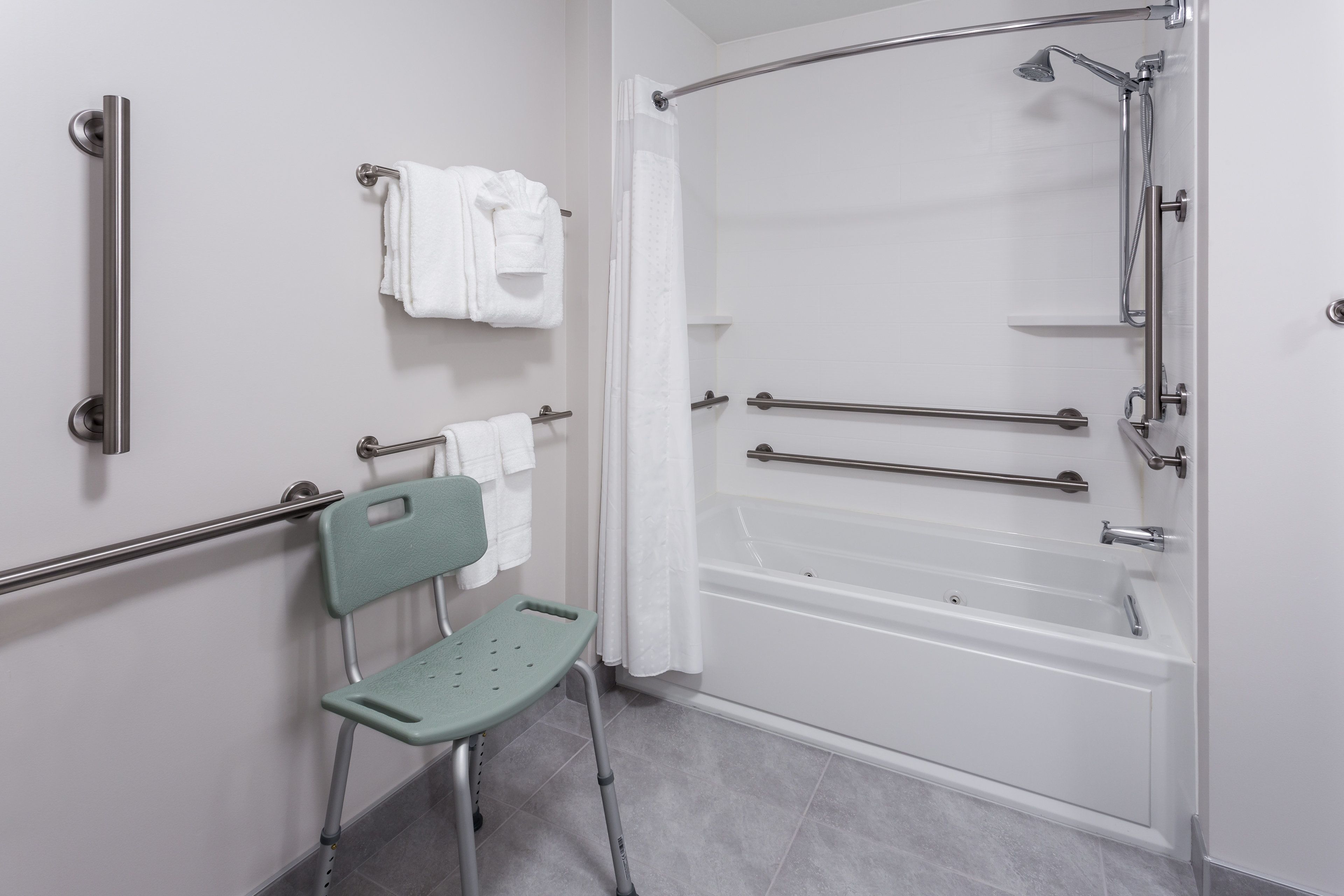 A bathroom with a walk-in shower, grab bars, a wheelchair-accessible chair, and a towel rack.