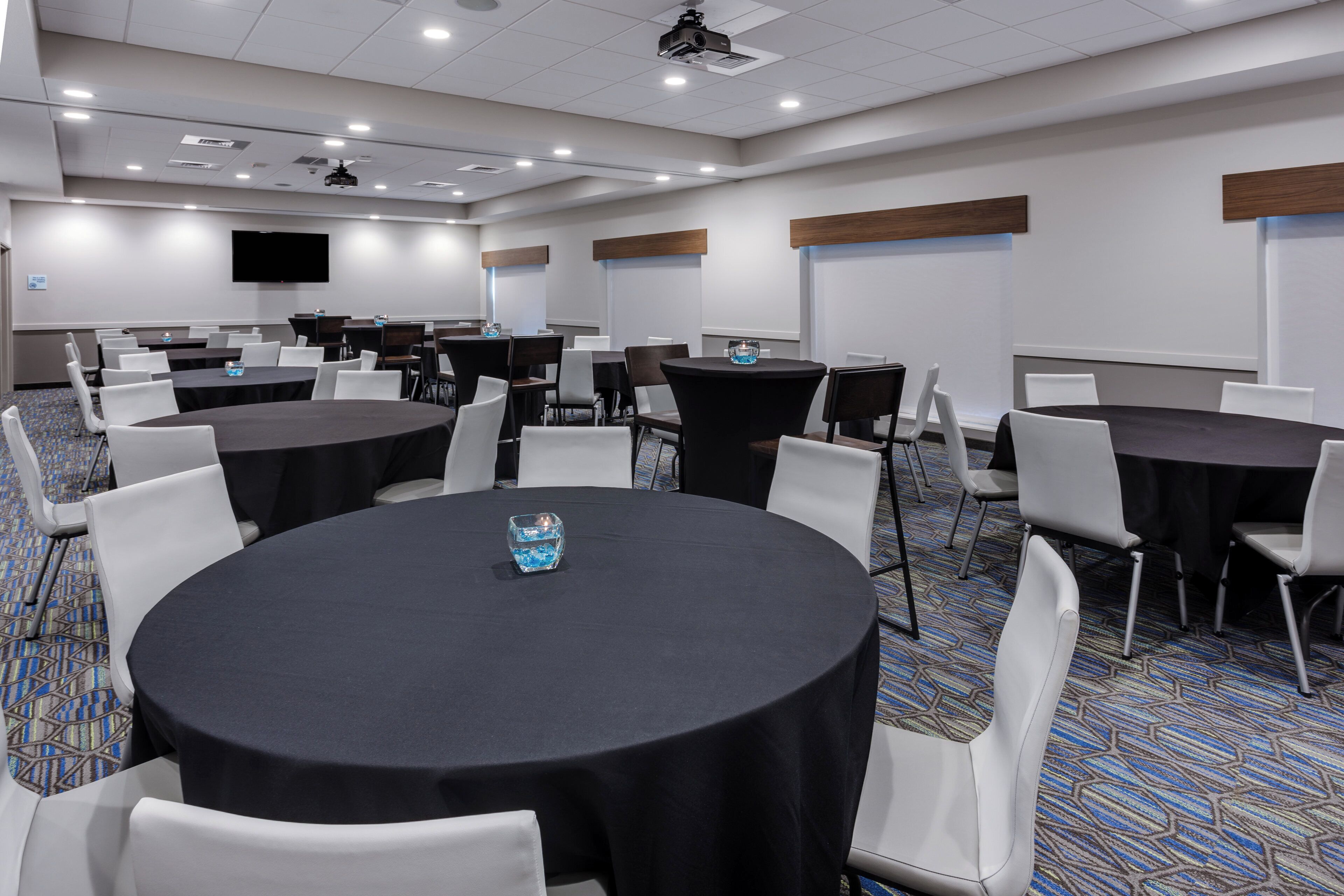 A conference room with multiple tables and chairs, a projector, and a flat-screen TV on the wall.
