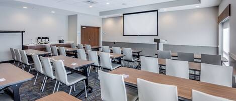 Une salle de conférence équipée de plusieurs tables et chaises, d’un projecteur et d’un écran.