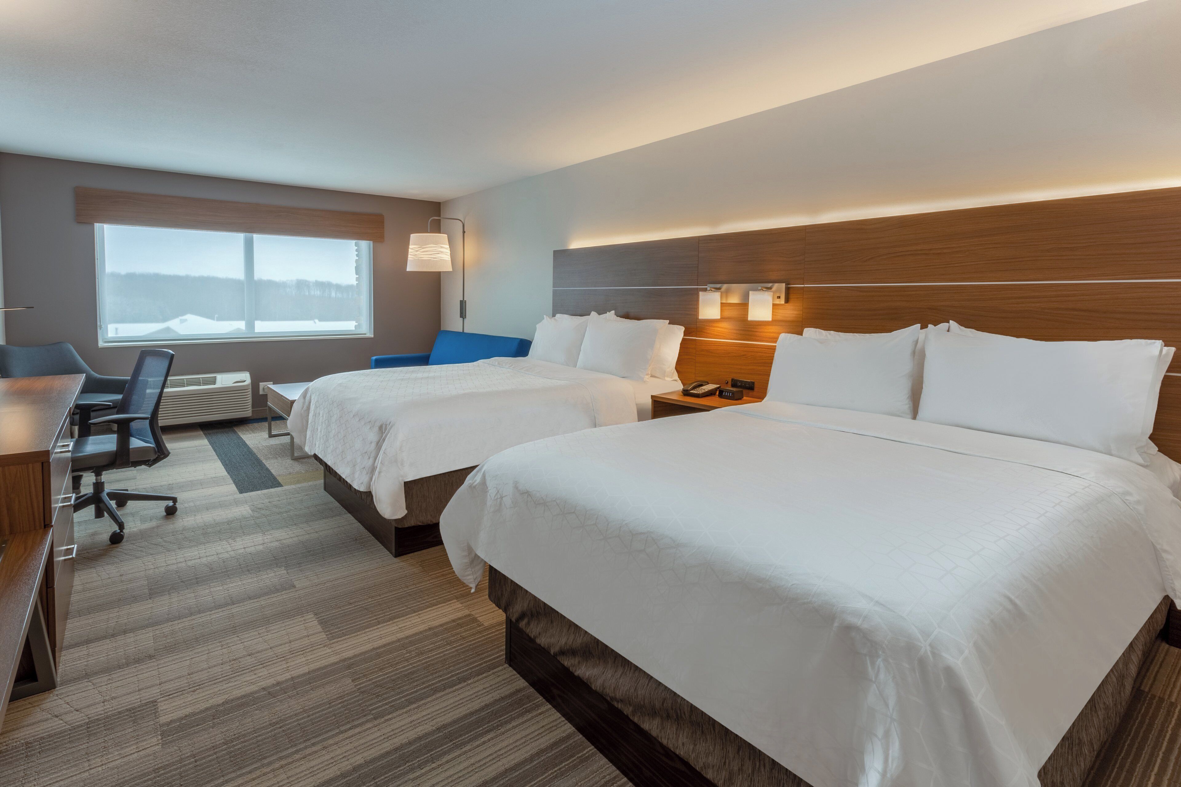 Habitación de hotel con dos camas, un escritorio, una silla, una lámpara y una ventana con vistas.
