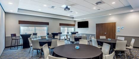 A conference room with multiple tables and chairs, a projector, and a large screen.
