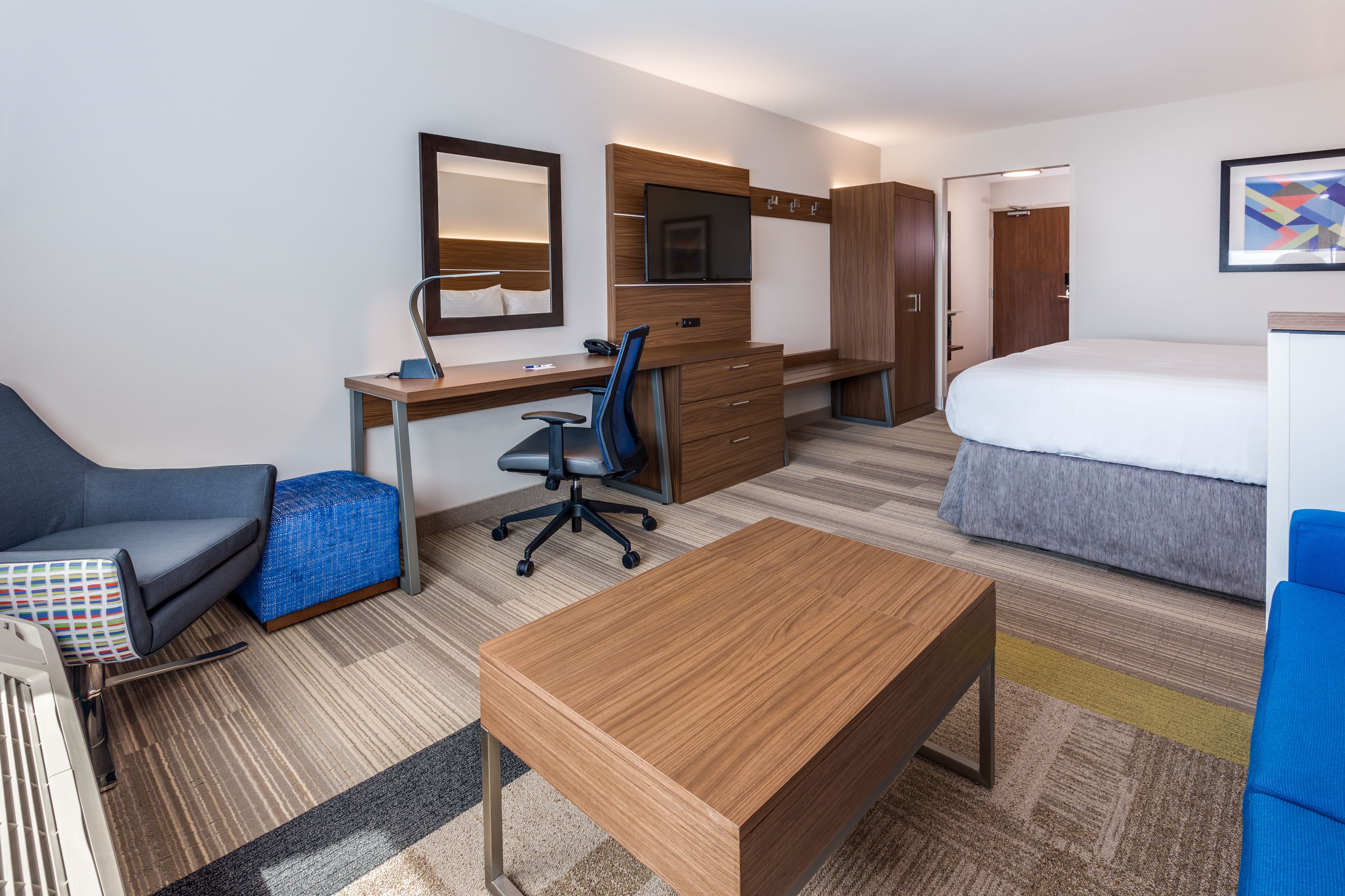 A hotel room with a bed, a desk with a chair, a wardrobe, and a TV mounted on the wall.