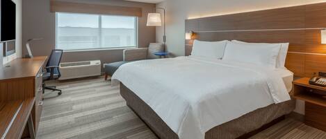 A hotel room with a large bed, a desk with a computer, a chair, a TV, and a window with a view.