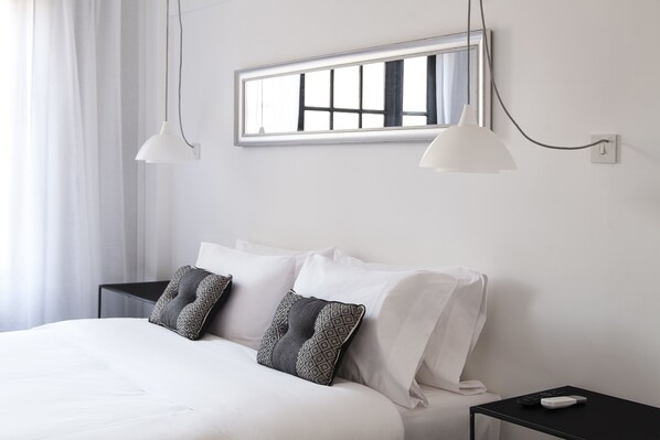 A neatly made bed with white linens and patterned pillows, a bedside table with a remote control, and a window with a view of the outside. - Hotel Alto San Isidro (San Isidro)