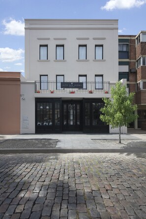 A two-story building with a sign reading "ALTO SARISIDRO". It features a flat facade, large windows, and a small balcony with railings. - Hotel Alto San Isidro (San Isidro)