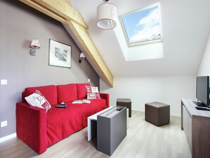 Une chambre de style loft moderne, avec un canapé rouge, un téléviseur, un bureau et une fenêtre de toit.