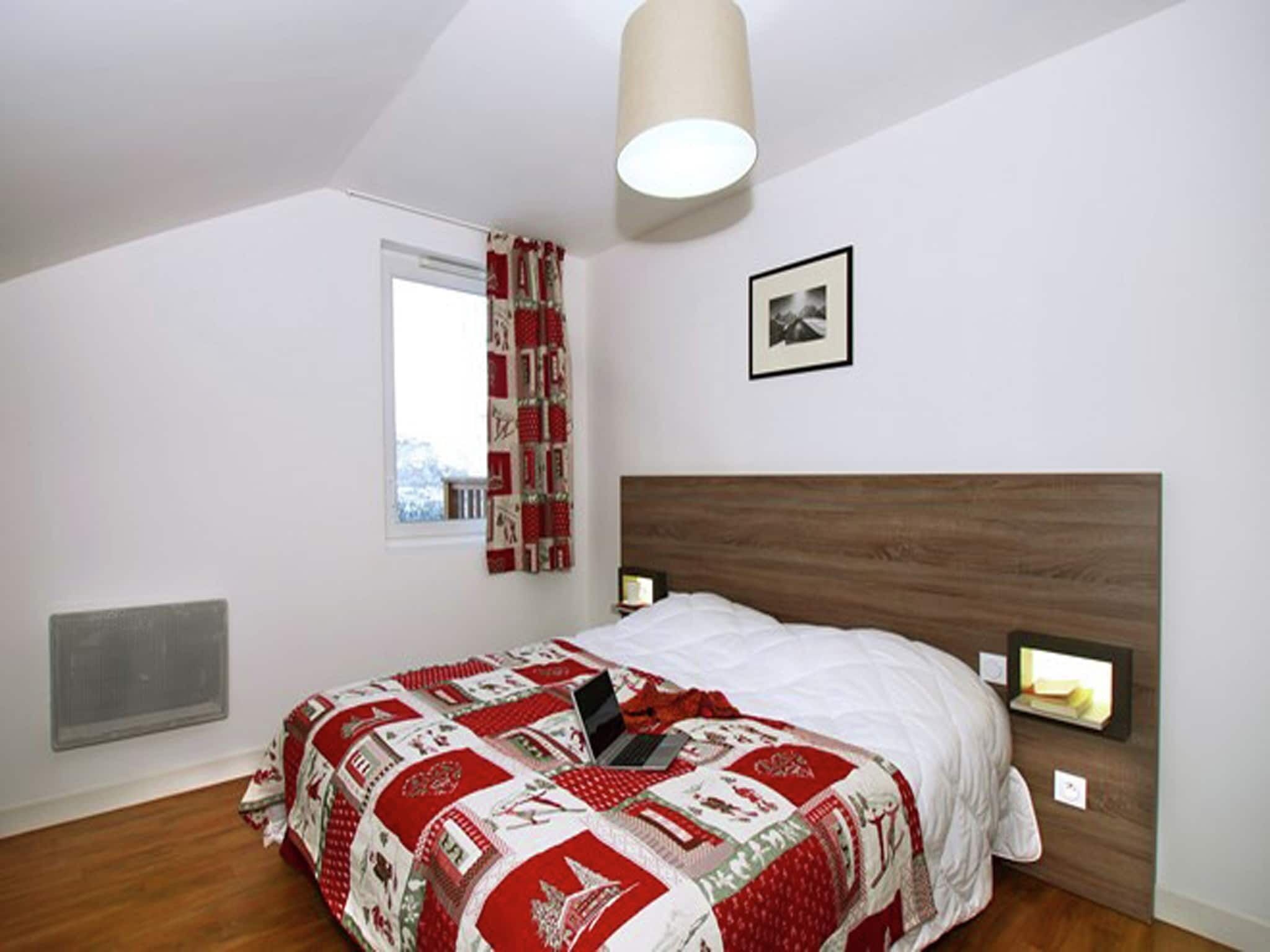 Une chambre à coucher avec un lit, une fenêtre avec des rideaux, un tableau au mur et un luminaire au plafond.