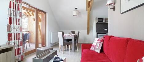 Una sala de estar moderna con un sofá rojo, un comedor con mesa y sillas, una cocina con microondas y un ventanal con cortinas.