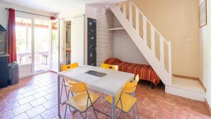 A room with a dining table and chairs, a staircase, and a bed with a striped blanket. - Villa in Poggio-Mezzana by the Beach (Poggio Mezzana)