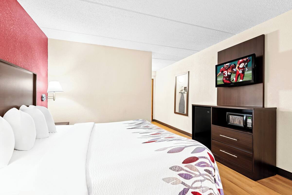 A hotel room with a large bed, a television mounted on the wall, a microwave, and a desk with drawers.