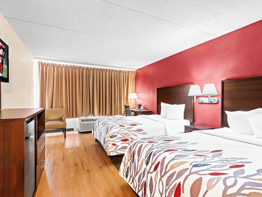 A hotel room with two beds, a desk, a chair, a TV, and a window with curtains.