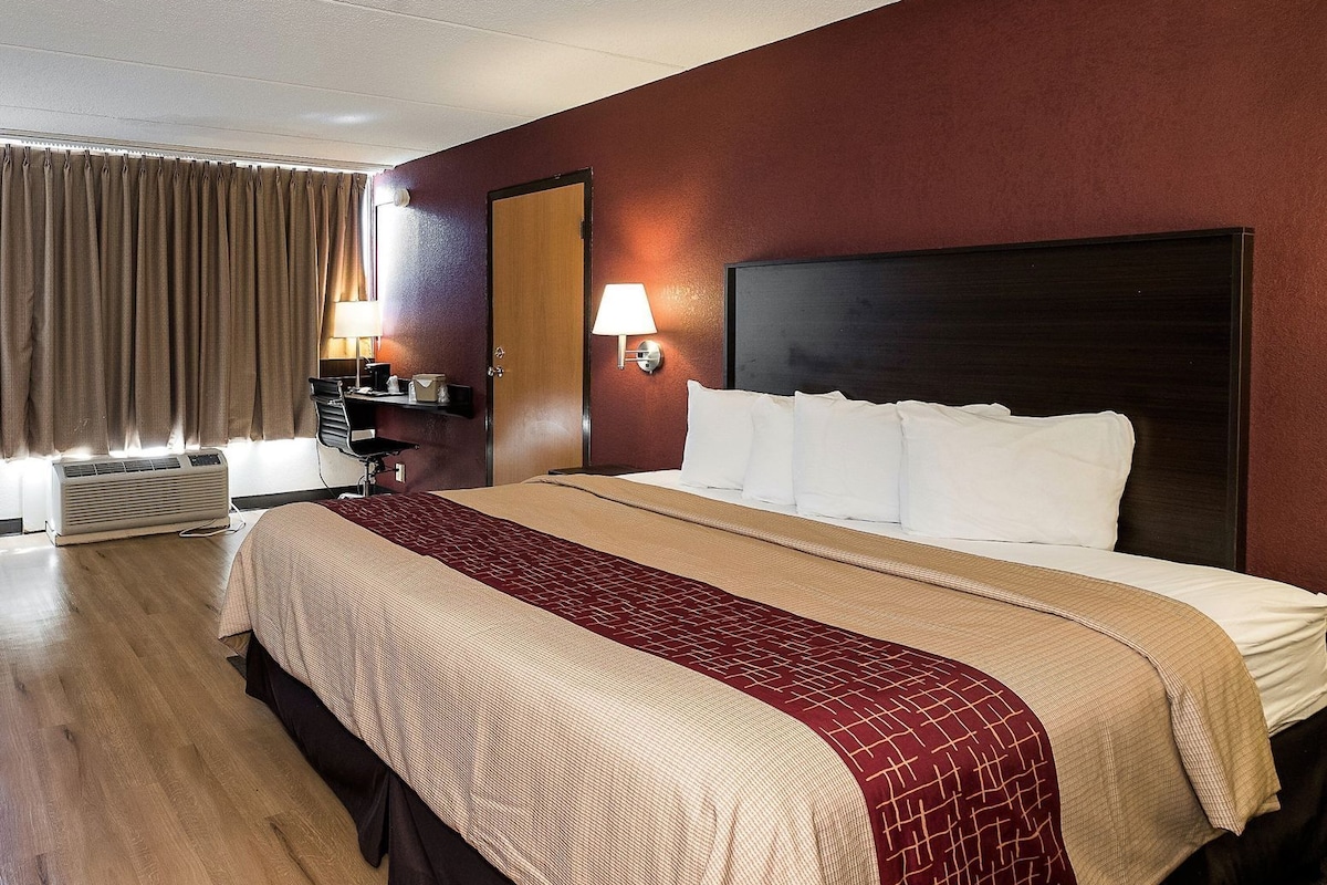 Una habitación de hotel con cama, escritorio, lámpara y ventana con cortinas.