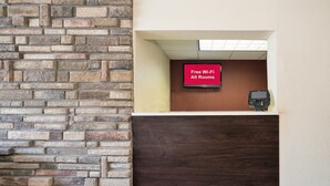 A reception area with a stone wall, a digital screen displaying 'Free Wi-Fi All Rooms,' and a payment terminal. - Red Roof Inn Cortland (Cortland)