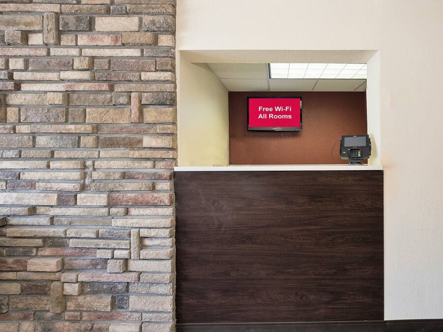 Ein Empfangsbereich mit einer Steinwand, einem digitalen Bildschirm mit der Aufschrift 'Kostenloses WLAN in allen Zimmern' und einem Zahlungsterminal.