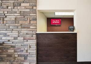 Una zona de recepción con una pared de piedra, una pantalla digital que muestra 'Wi-Fi gratuito en todas las habitaciones' y un terminal de pago.