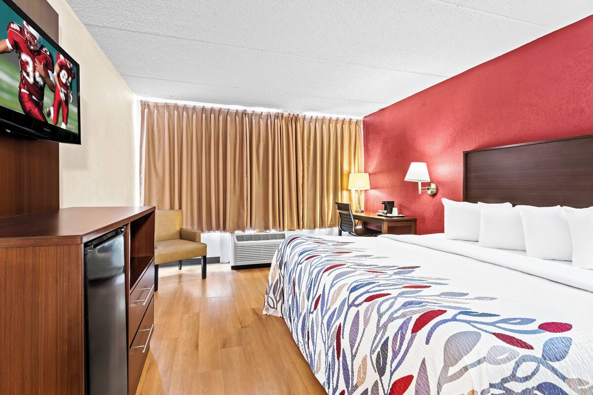 A hotel room with a bed, a desk, a chair, a television, and a window with curtains.