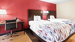 Ett hotellrum med en röd vägg, ett skrivbord med en stol, två sängar med vita sängkläder och ett mönstrat överkast.