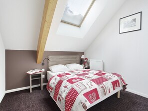 A bedroom with a sloped ceiling, a bed with a red and white quilt, a bedside table with a lamp, and a framed picture on the wall.