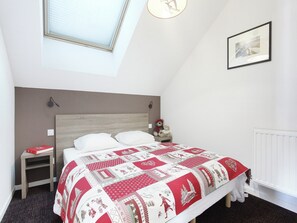 Ein Schlafzimmer mit einem Bett, einem Nachttisch, einem Teddybären, einem gerahmten Bild und einem Fenster.