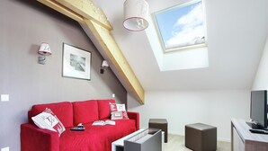 A modern loft bedroom with a red sofa, a TV, and a skylight. - Apartment in French Alps with Heated Pool (La Salle les Alpes)