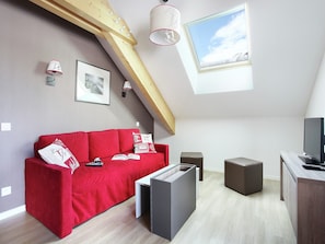 Ein modernes Schlafzimmer im Loft-Stil mit einem roten Sofa, einem Fernseher und einem Dachfenster.