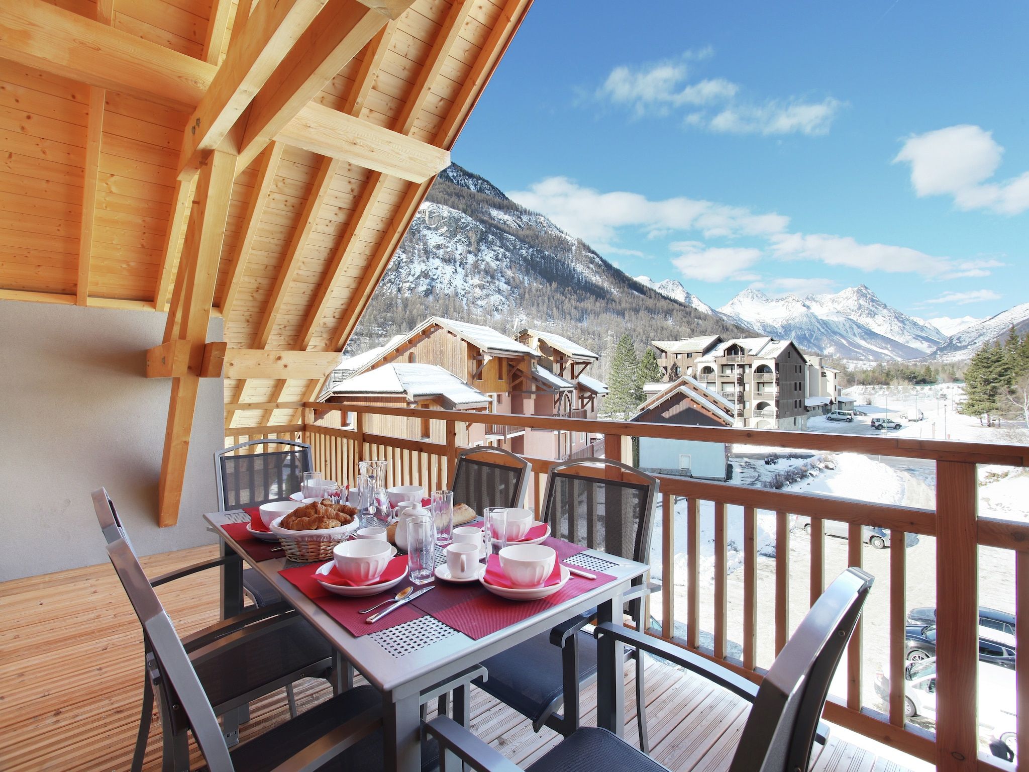 Une terrasse en bois avec une table dressée pour le petit-déjeuner, offrant une vue sur un paysage montagneux.