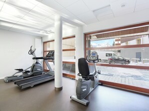 A gym with treadmills and an elliptical machine, large windows with a view of a snowy landscape and parked cars.