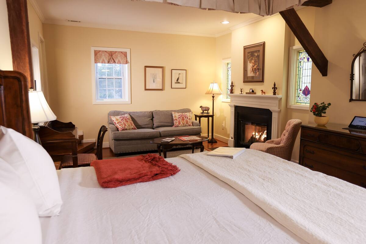 A hotel room with a bed, a sofa, a fireplace, and a desk.