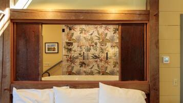 Habitación de hotel con cabecera de madera, un espejo grande y cortina de ducha con estampado tropical.