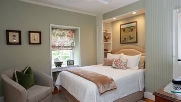A bedroom with a bed, a chair, a window with curtains, a ceiling fan, and a painting on the wall.