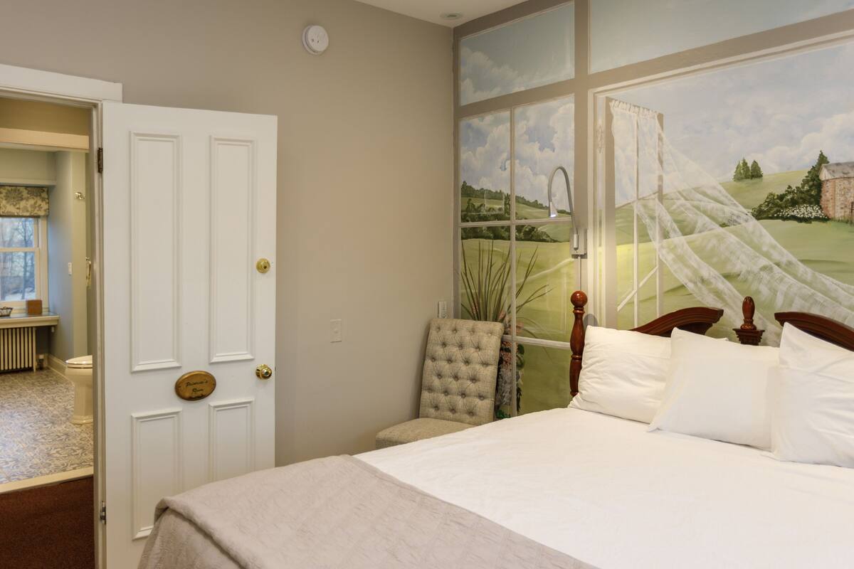 A bedroom with a large window, a bed with white linens, a chair, and a door leading to another room.