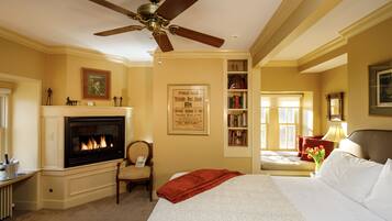 A hotel room with a fireplace, a bed, a bookshelf, and a ceiling fan.