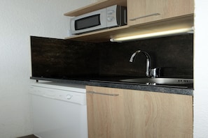 A compact kitchen with a built-in microwave, a stainless steel sink, and a dishwasher. - Cozy Retreat in Les Allues (Les Allues)