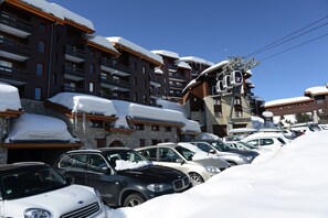 A snow-covered parking lot with cars and a building with balconies and a ski lift. - Cozy Retreat in Les Allues (Les Allues)