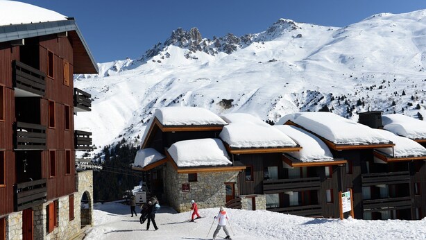 Een bergchalet bedekt met sneeuw, met houten architectuur en skipistes op de achtergrond.