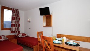 Een kamer met twee eenpersoonsbedden, een houten ontbijttafel, een aan de muur bevestigde televisie en een raam met gordijnen.