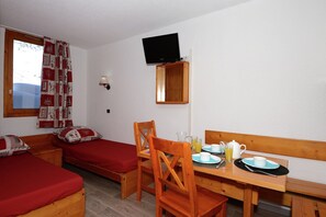 Ein Zimmer mit zwei Einzelbetten, einem Holztisch, der für das Frühstück gedeckt ist, einem an der Wand befestigten Fernseher und einem mit Vorhängen versehenen Fenster.