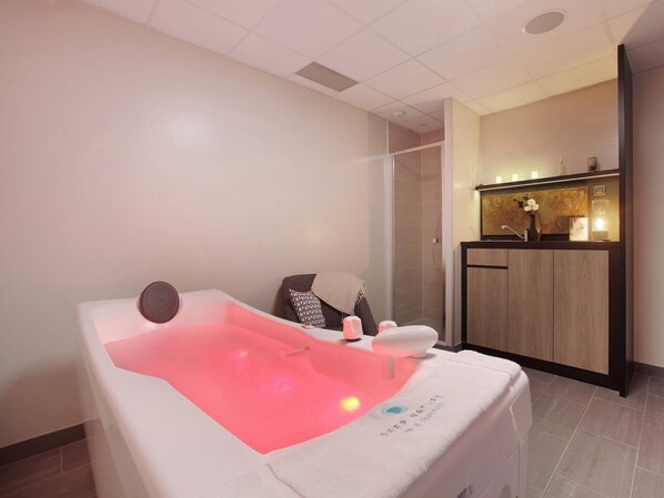 Une salle de spa équipée d’une table de massage, d’un petit lavabo et d’une coiffeuse avec un miroir.