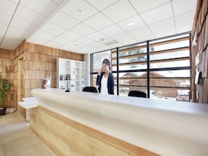 A reception desk with a wooden panel wall, a white shelving unit, and a large window with a view of snow-covered buildings.