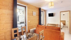 Tunnelmallinen huone, jossa on ruokapöytä katettuna, sohva, televisio ja näkymä ulos.