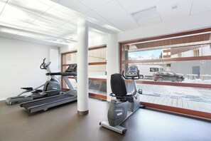 Ein Fitnessstudio mit Laufbändern und einem Crosstrainer, große Fenster mit Blick auf eine verschneite Landschaft und parkende Autos.